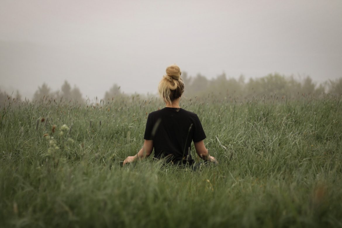 Frau sitzt mitten auf einer Wiese und meditiert